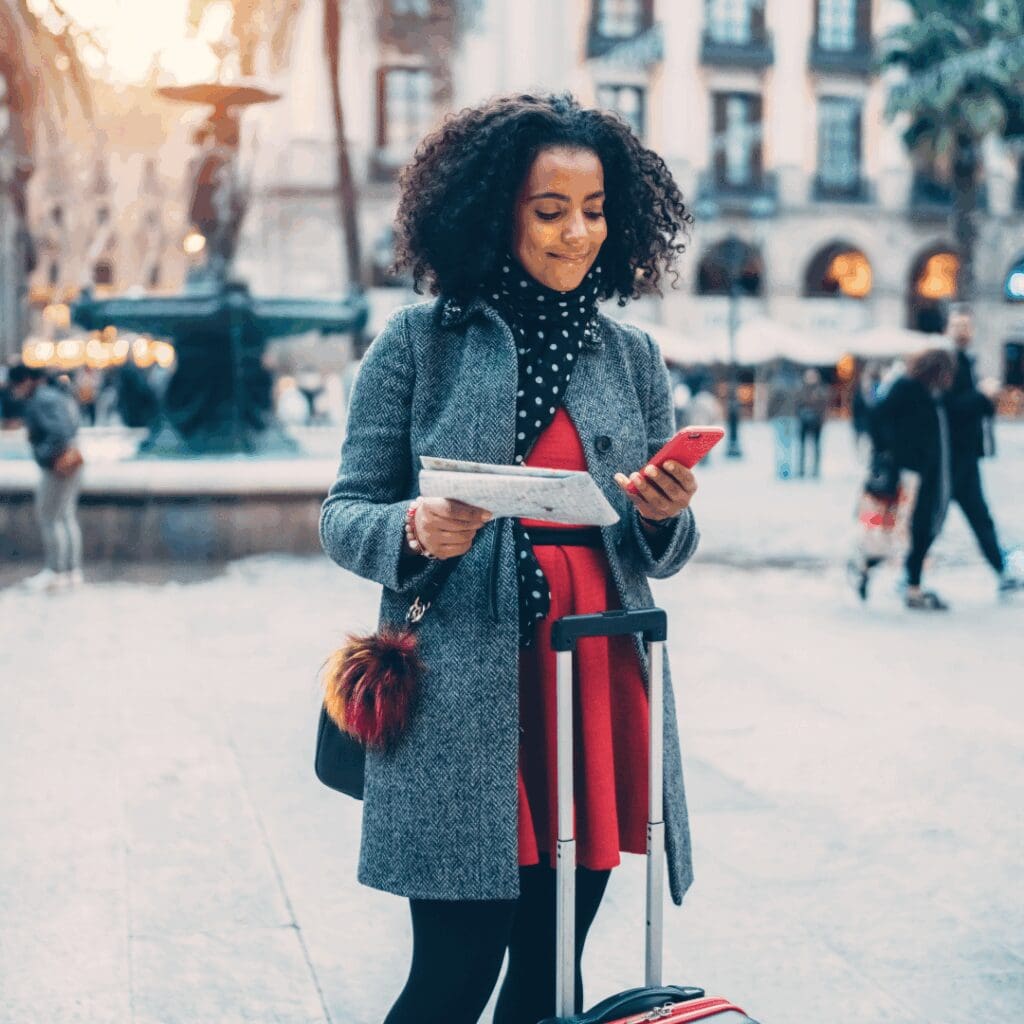 Smiling Black woman solo traveler exploring a European city with a suitcase, paper map, and phone in hand—confident, prepared, and enjoying the adventure.
