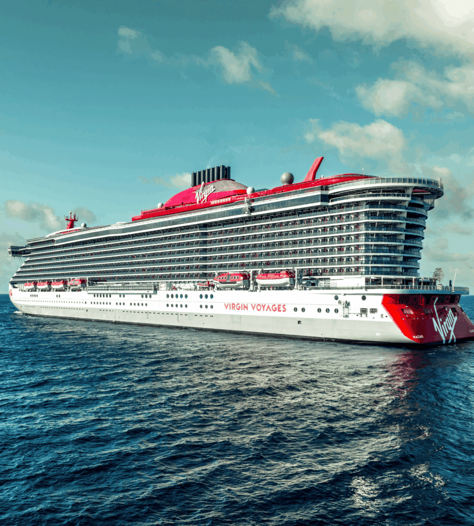 Virgin Voyages cruise ship sailing at sea on a sunny day, showcasing the ship’s signature red and white design and multiple balcony cabins.
